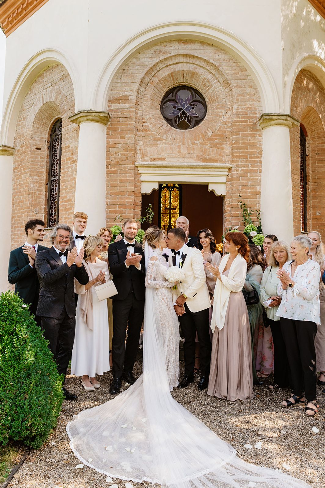 Wedding party gathered outside a brick church with elegant floral arrangements and white decor.
