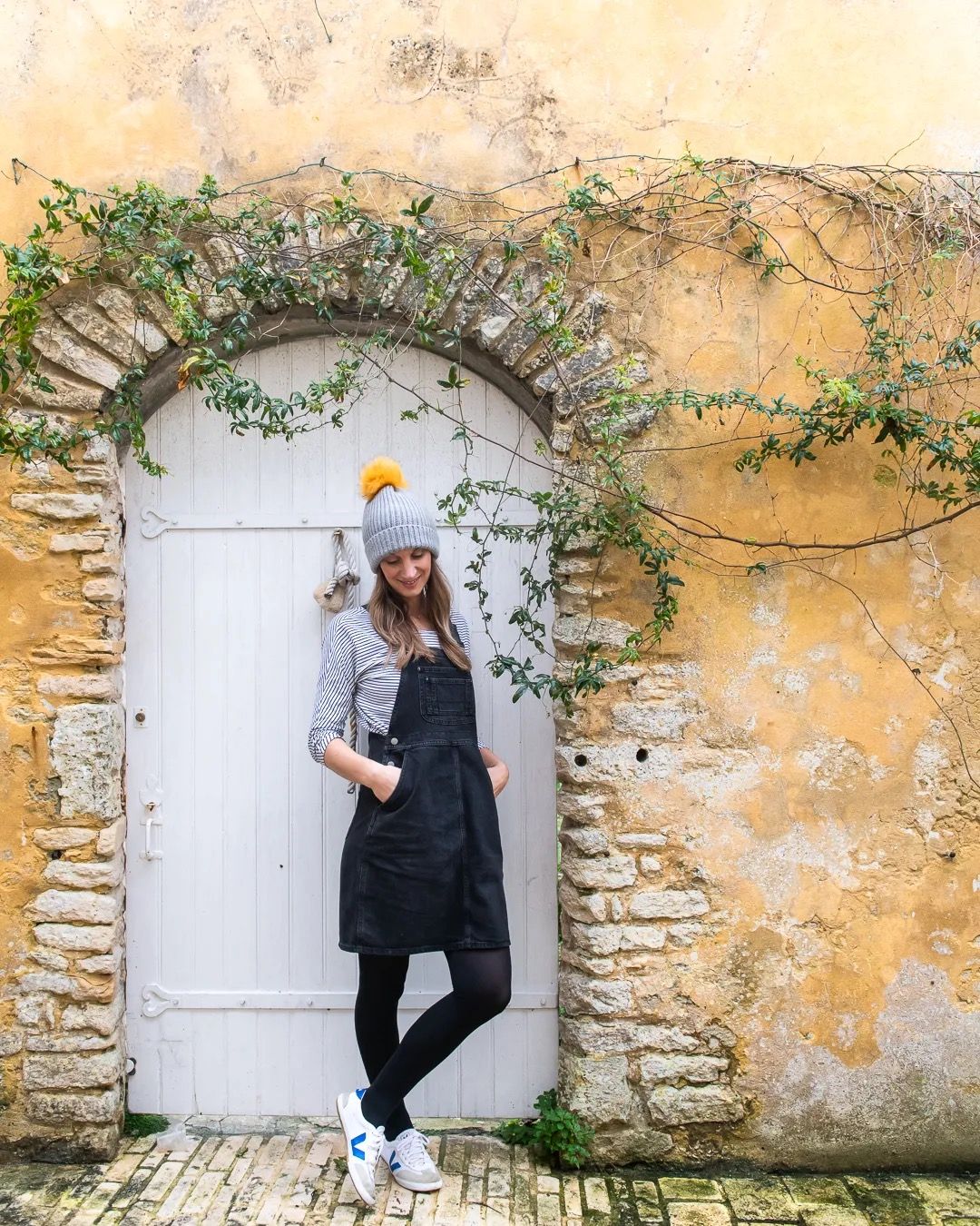 A woman standing by a rustic stone archway covered in climbing vines.
