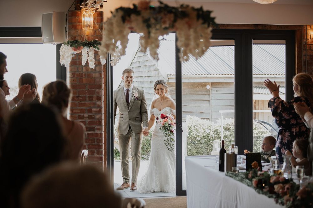 Bride and groom making their grand entrance into the wedding reception through a floral arch doorway.