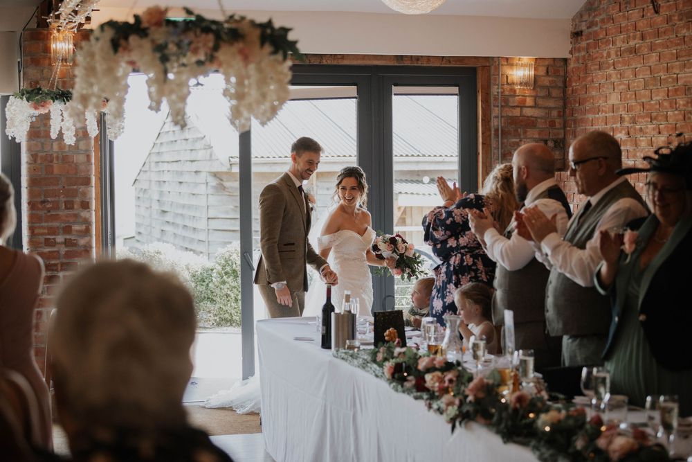 Bride and groom enter wedding reception hall greeted by applauding guests at elegantly decorated venue.