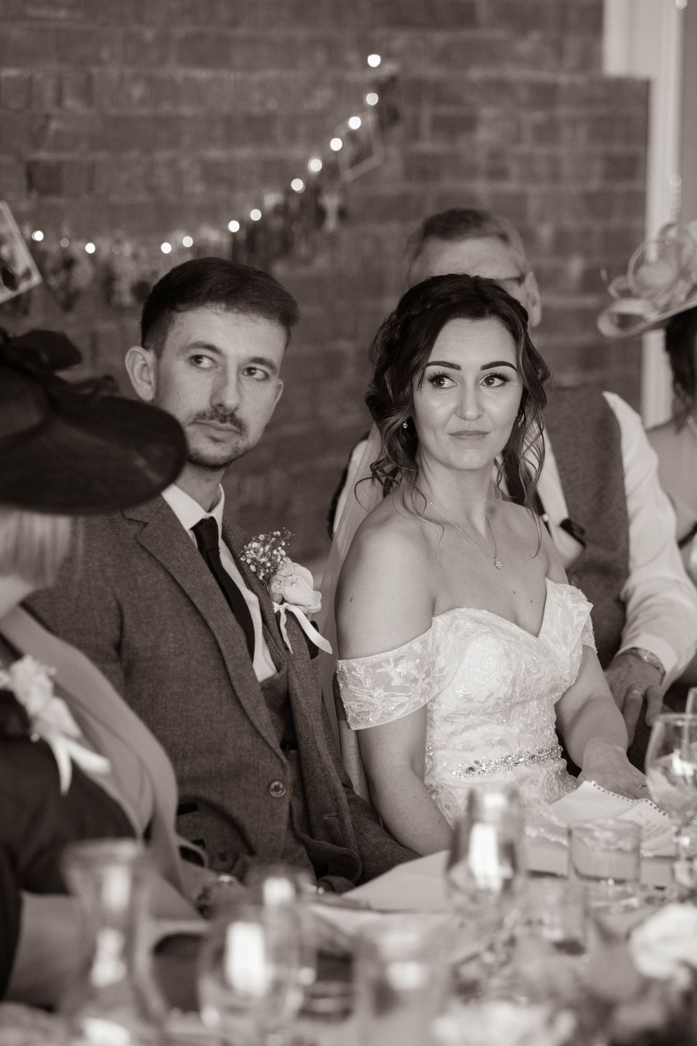 Black and white portrait of bride and groom listening attentively at wedding reception table.