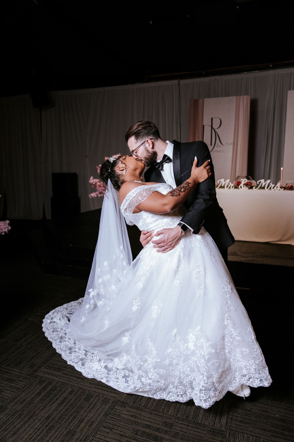 A romantic wedding couple shares a dramatic dip kiss on the dance floor with the bride's lace gown flowing elegantly.