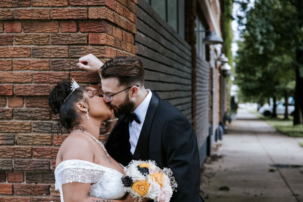 A romantic wedding couple shares intimate moments against a rustic brick wall backdrop during their special day.