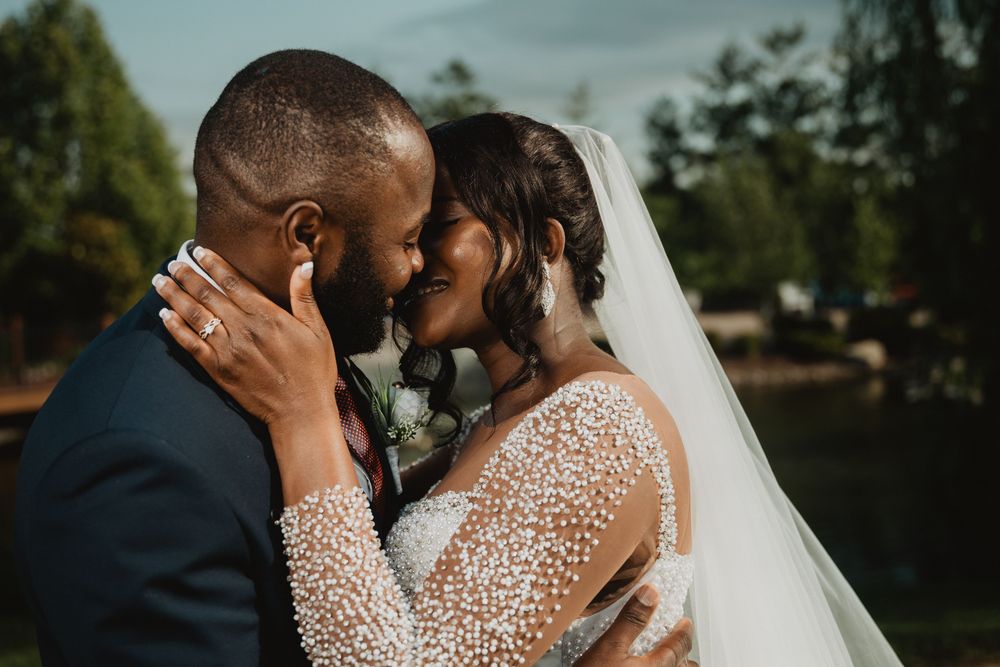 Intimate wedding couple shares romantic kisses in a garden setting with trees in the background.