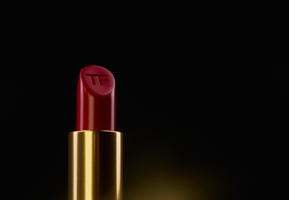 Luxurious red lipstick with gold base photographed on black background with dramatic lighting.
