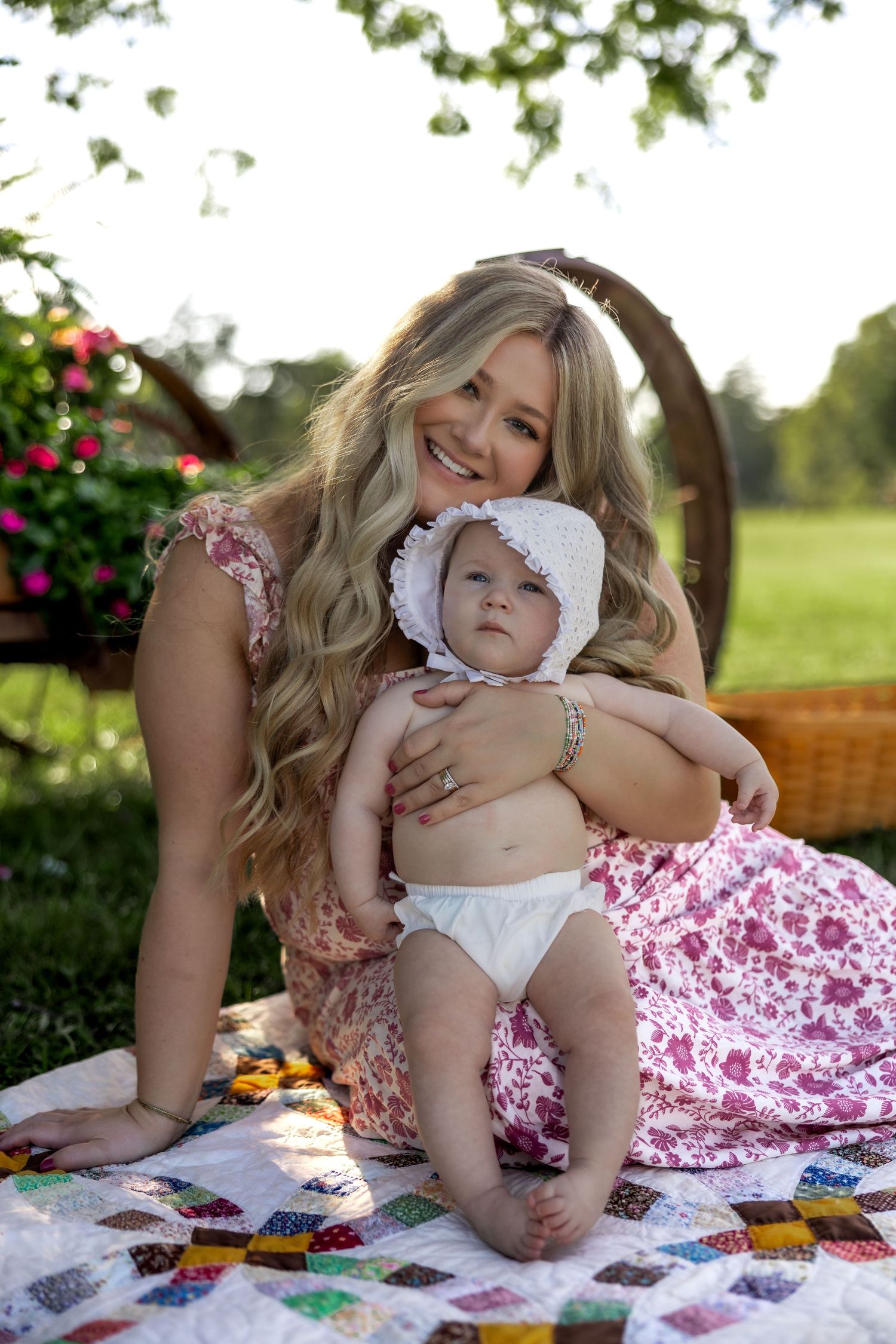 Sweet outdoor portrait of mother and baby relaxing together on a patchwork quilt in a garden setting.