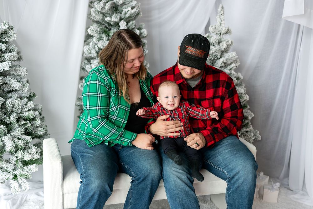Parents in green and red plaid shirts looking down at smiling baby during Christmas photo session.
