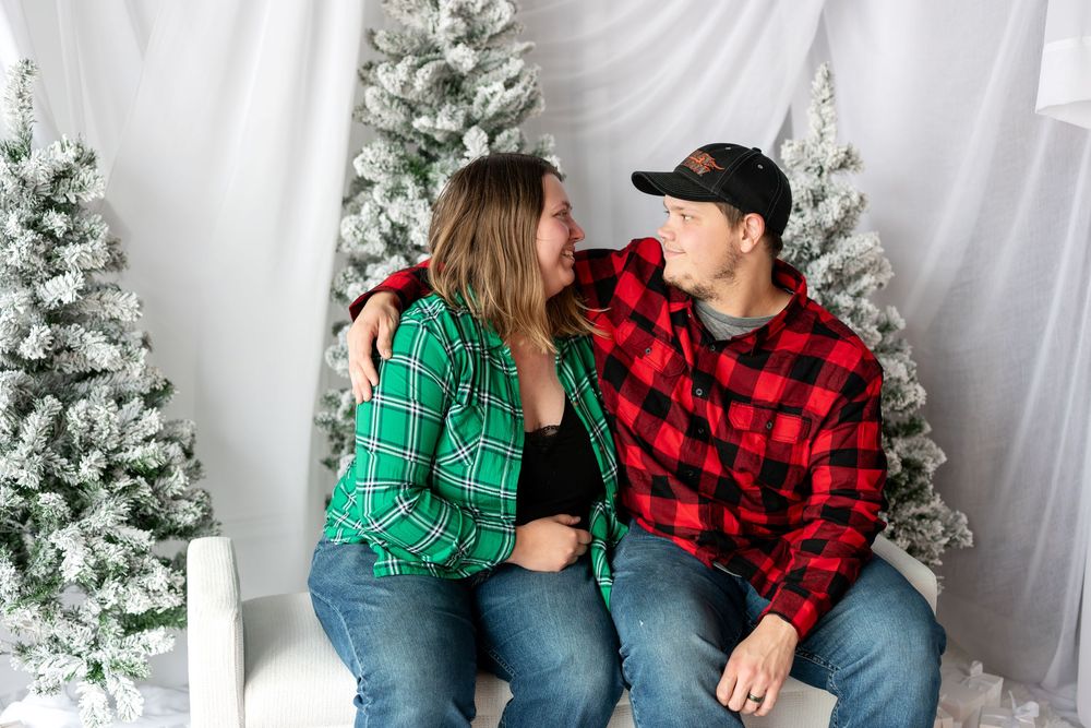 Young couple in plaid shirts gazing at each other lovingly during Christmas mini session.