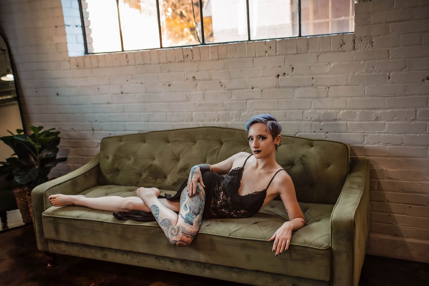 Boudoir Photography of a woman with tattoos wearing a black gown, lounging on a green couch in Salt Lake studio