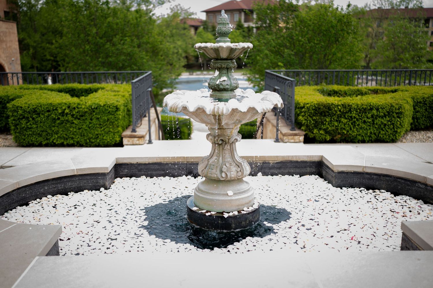 Ornate stone fountain surrounded by white pebbles and manicured hedges in a formal garden setting at the club at corazon