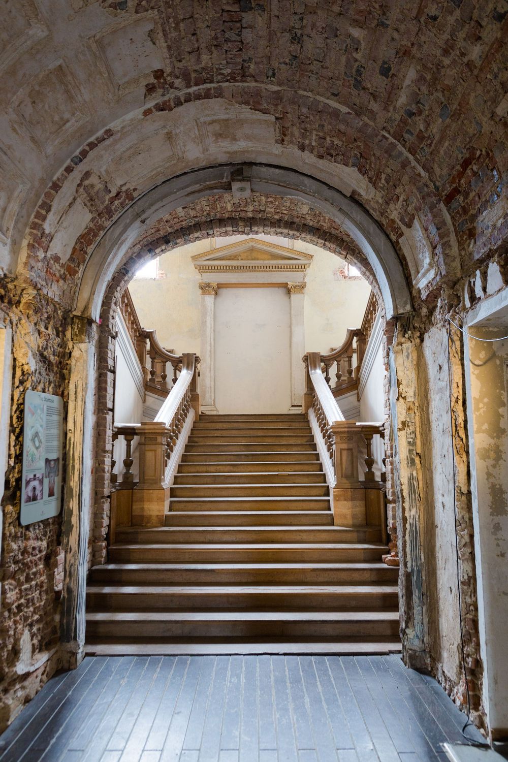 Stone archway leads to elegant marble staircase with ornate wooden railings in historic building interior.