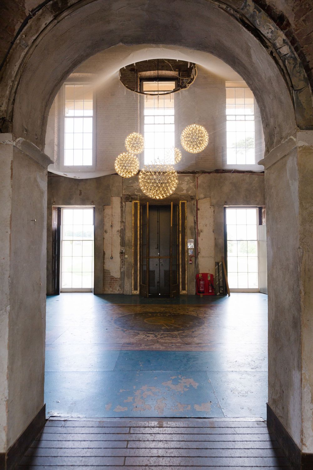 Interior view of an empty historic room with arched ceilings, hanging sphere lights, and tall windows letting in natural light.