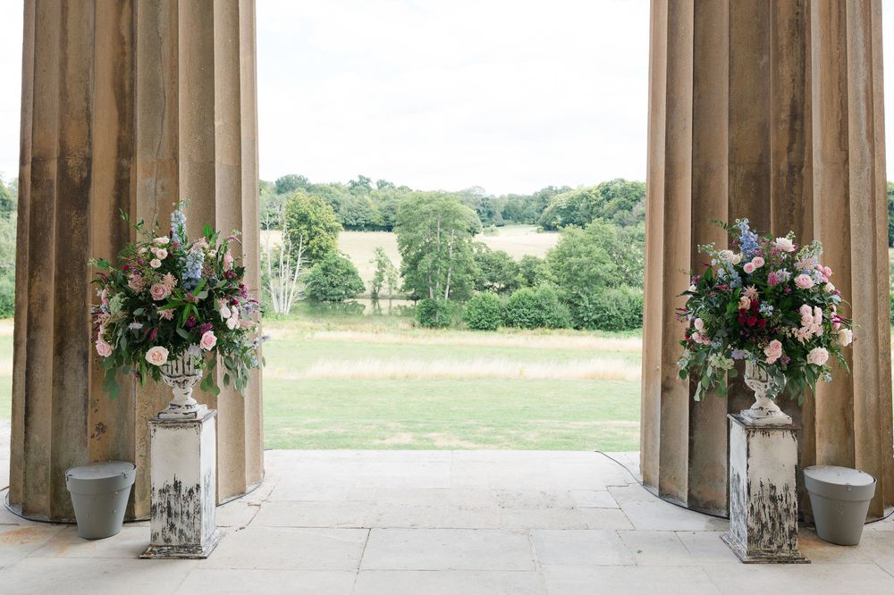 Elegant wedding venue interior with tall wooden columns and hanging floral arrangements along a stone walkway.