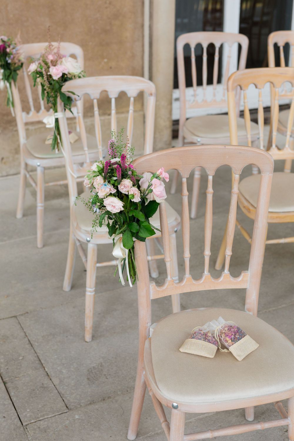 White vintage chairs decorated with delicate pink and purple floral arrangements line up for an elegant wedding ceremony.