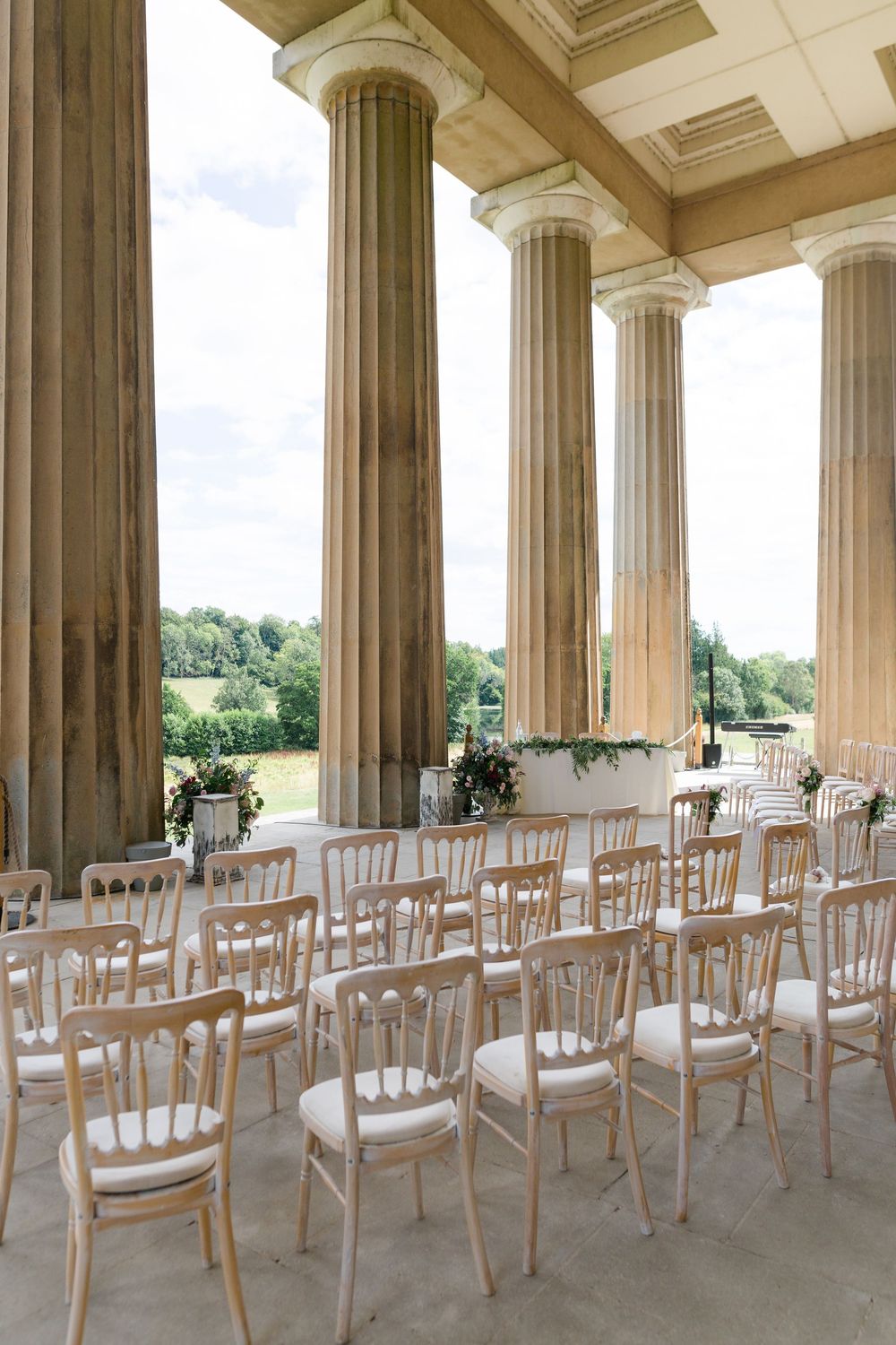 White wooden chairs arranged in rows under a grand columned portico for an elegant outdoor ceremony setup.