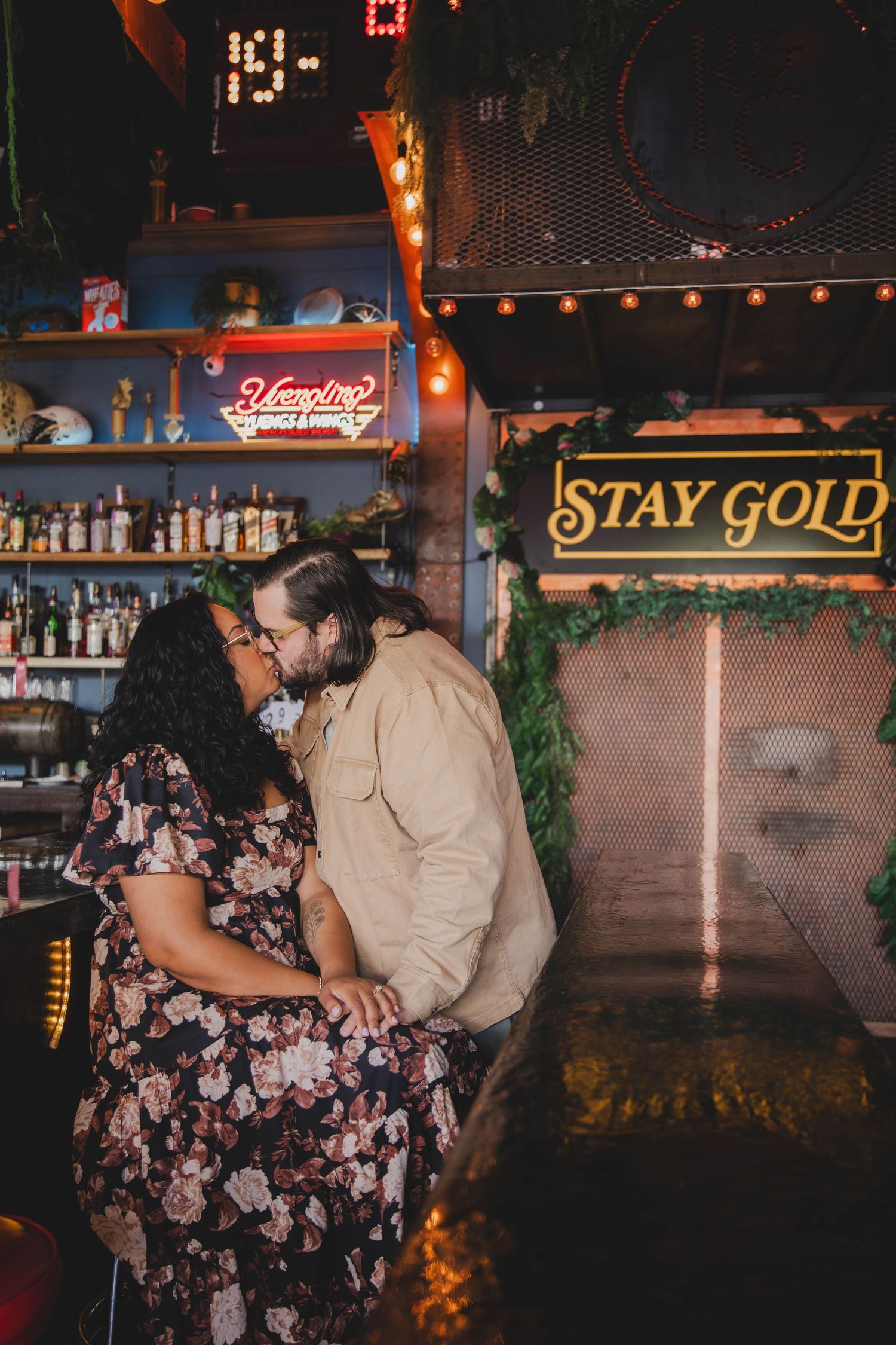 Couple kissing in a bar with Stay Gold neon sign.