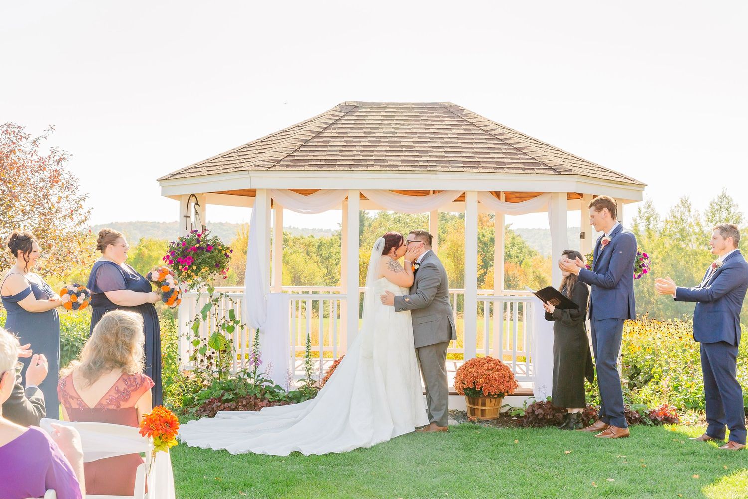 Wedding party gathers at sunset near white gazebos and autumn decorations during outdoor celebration.
