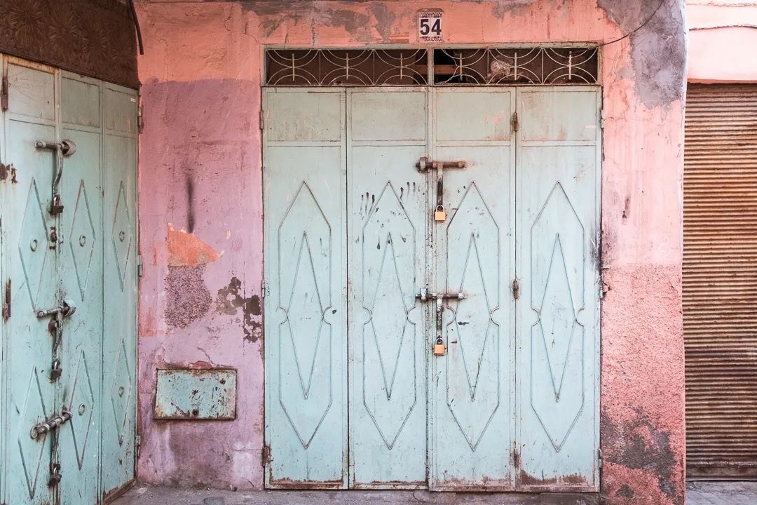 A pair of mint green carved Moroccan doors in a narrow alley with soft pastel walls.