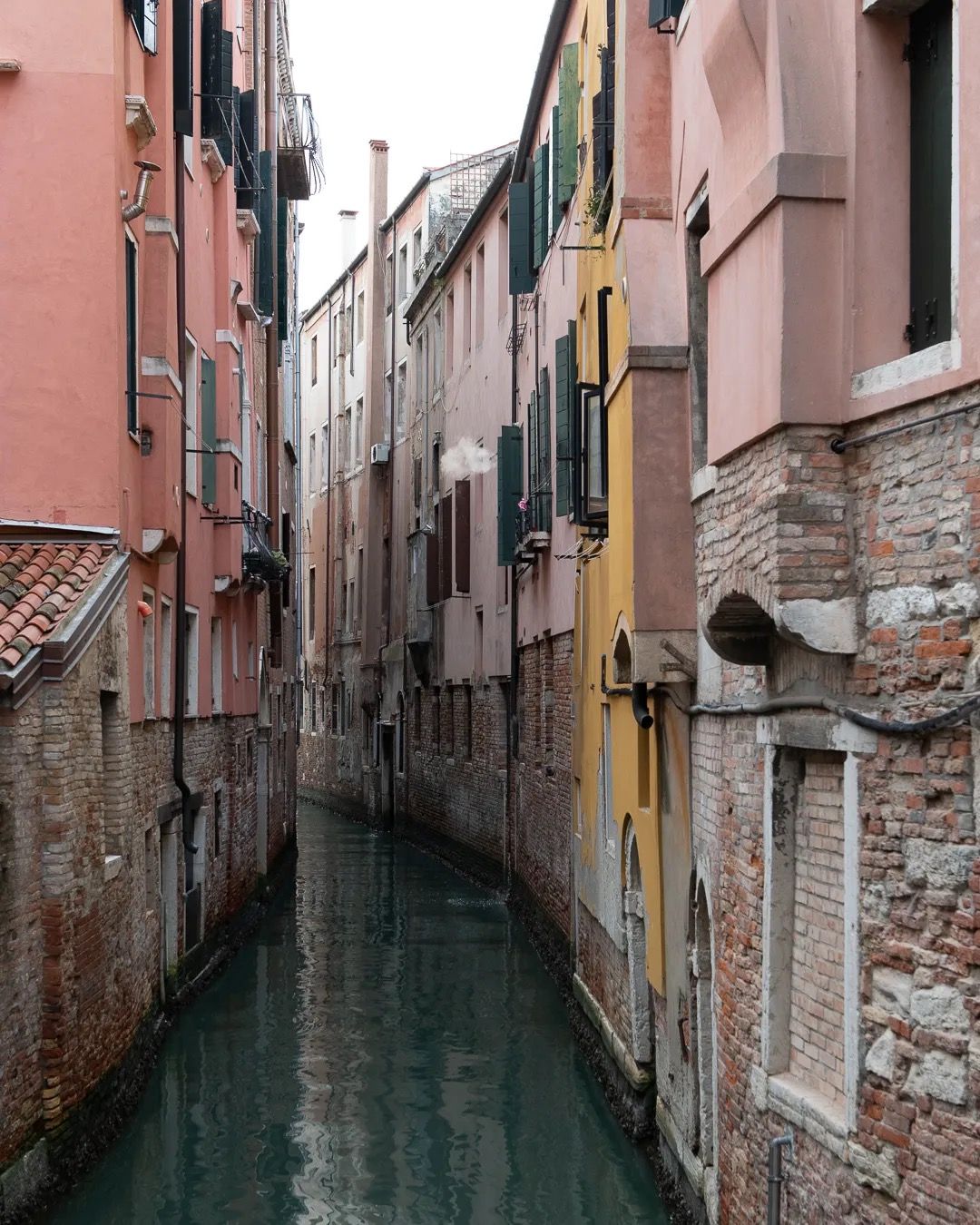 Peaceful Venice canal framed by pastel buildings with still turquoise water.