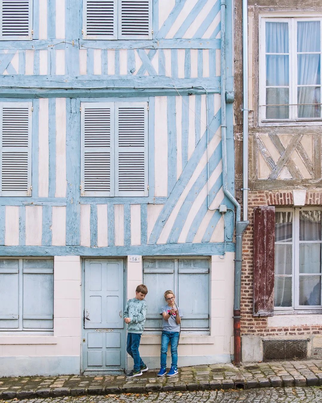 Family standing outside a blue timber-frame house in a charming French village.