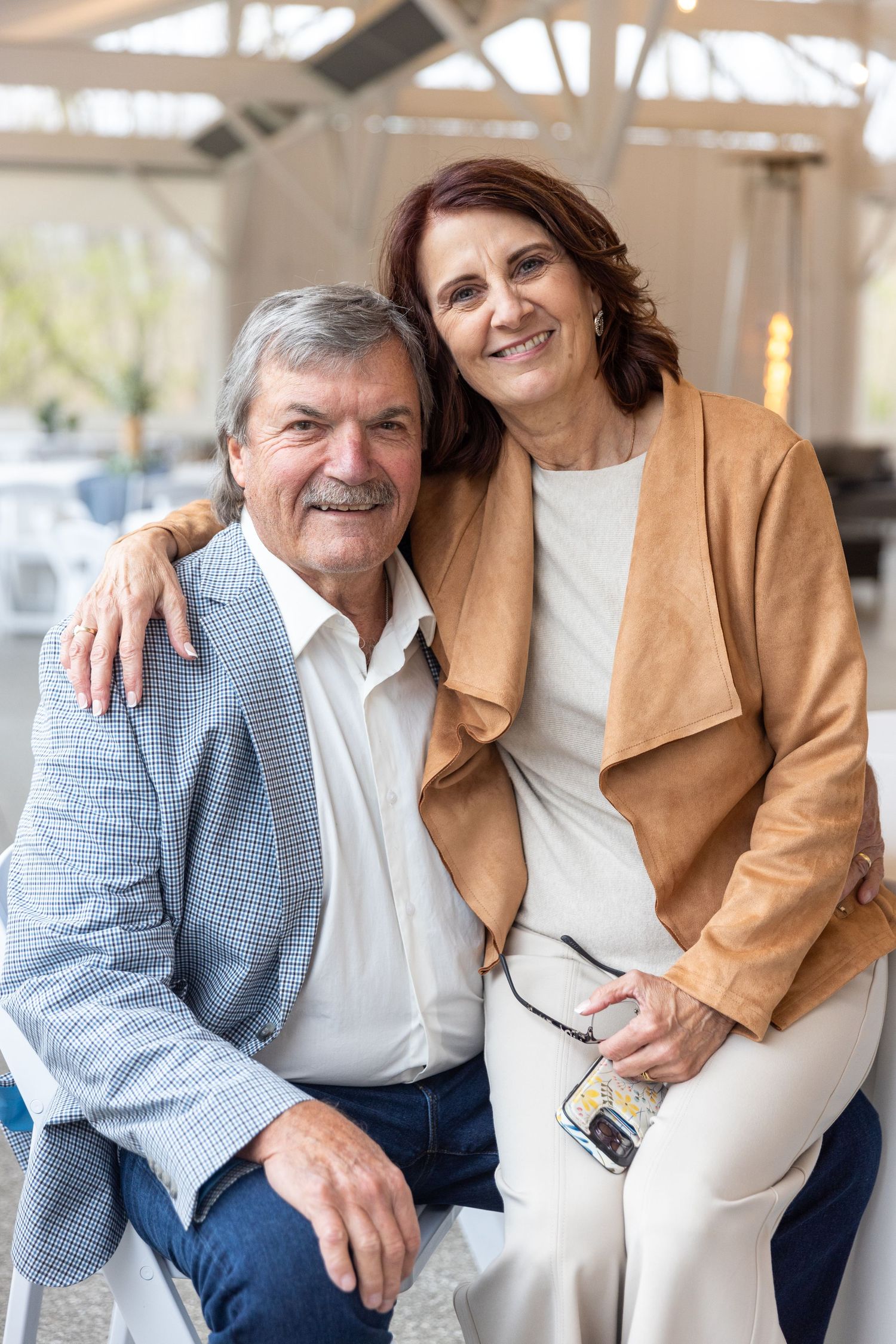 Two people sitting close together on a porch, one wearing a tan jacket and the other in casual attire.