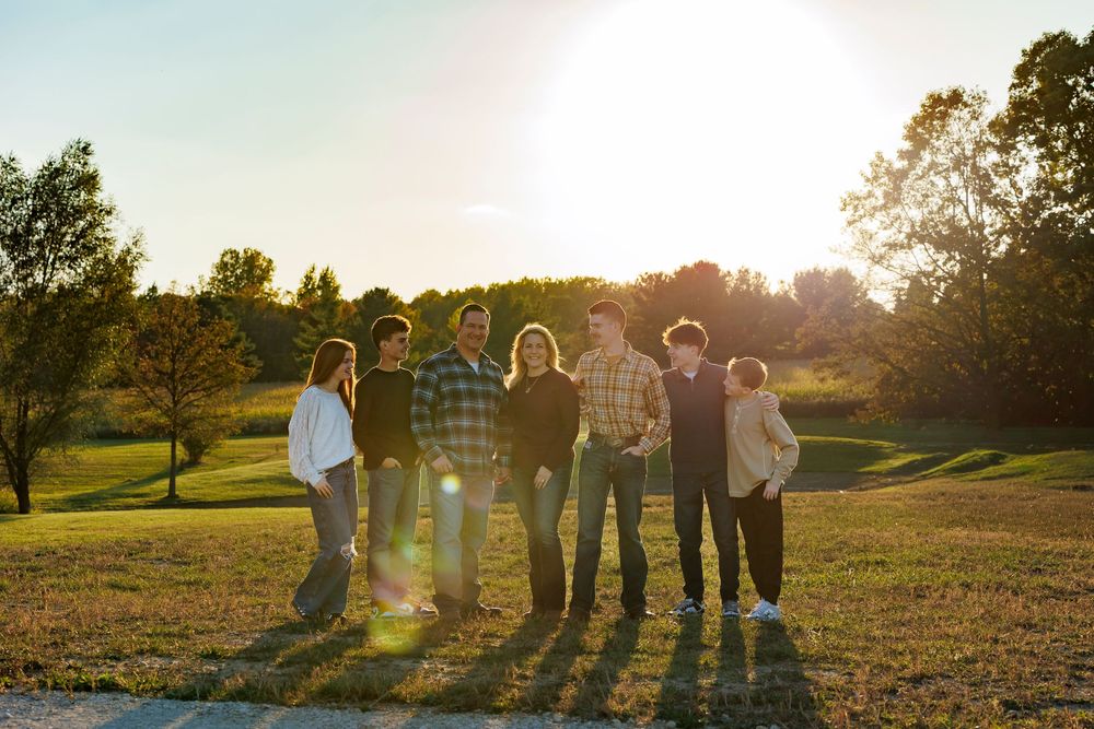 Group of people standing together in a golden field at sunset with long shadows cast behind them.