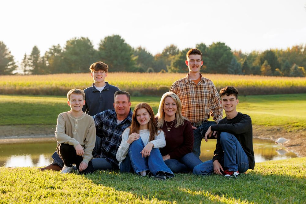 Family group sits together on grassy hill during golden hour sunset photography session.