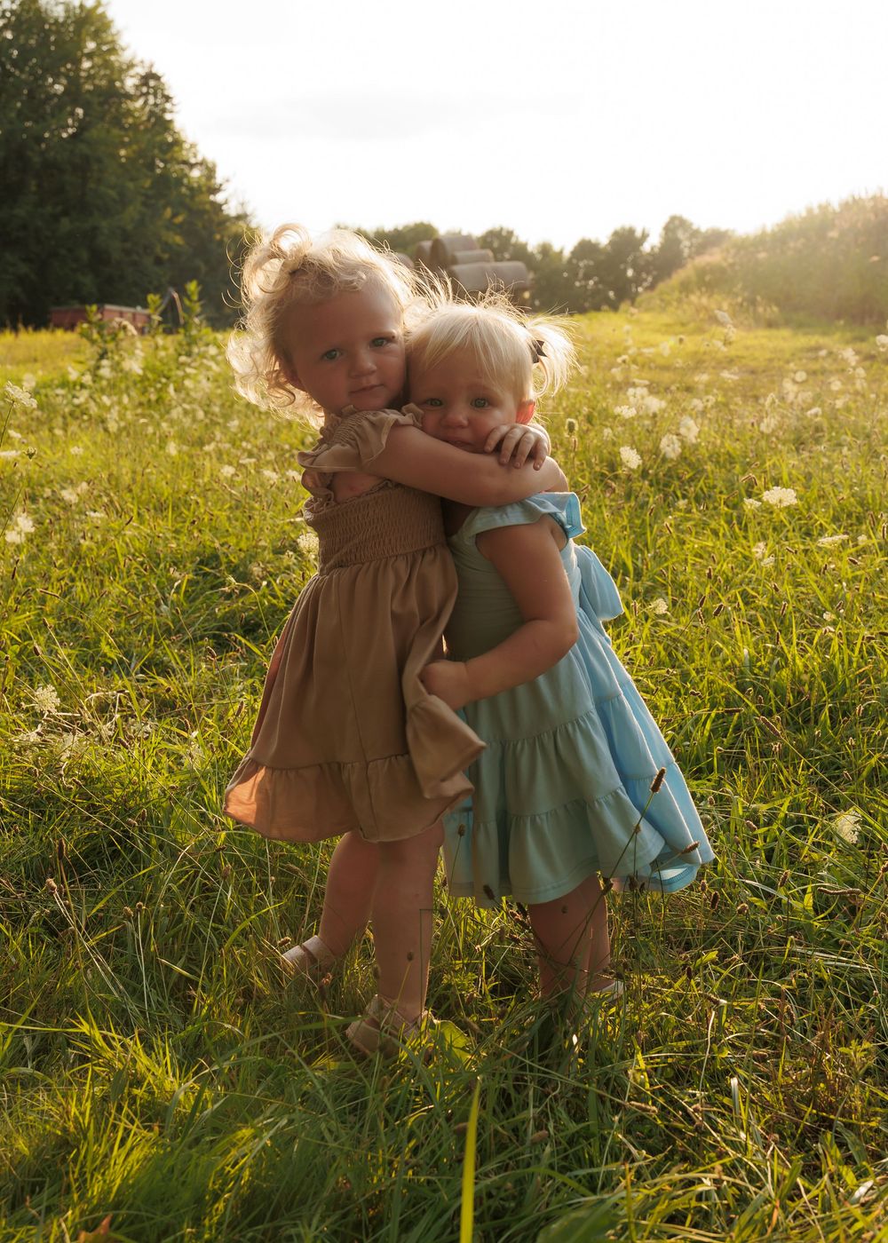 Two children embrace in a sunlit meadow filled with wildflowers during golden hour.