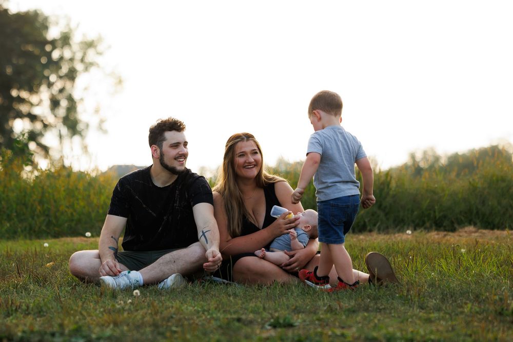 Family relaxing together on grassy hill during golden hour sunset in nature.