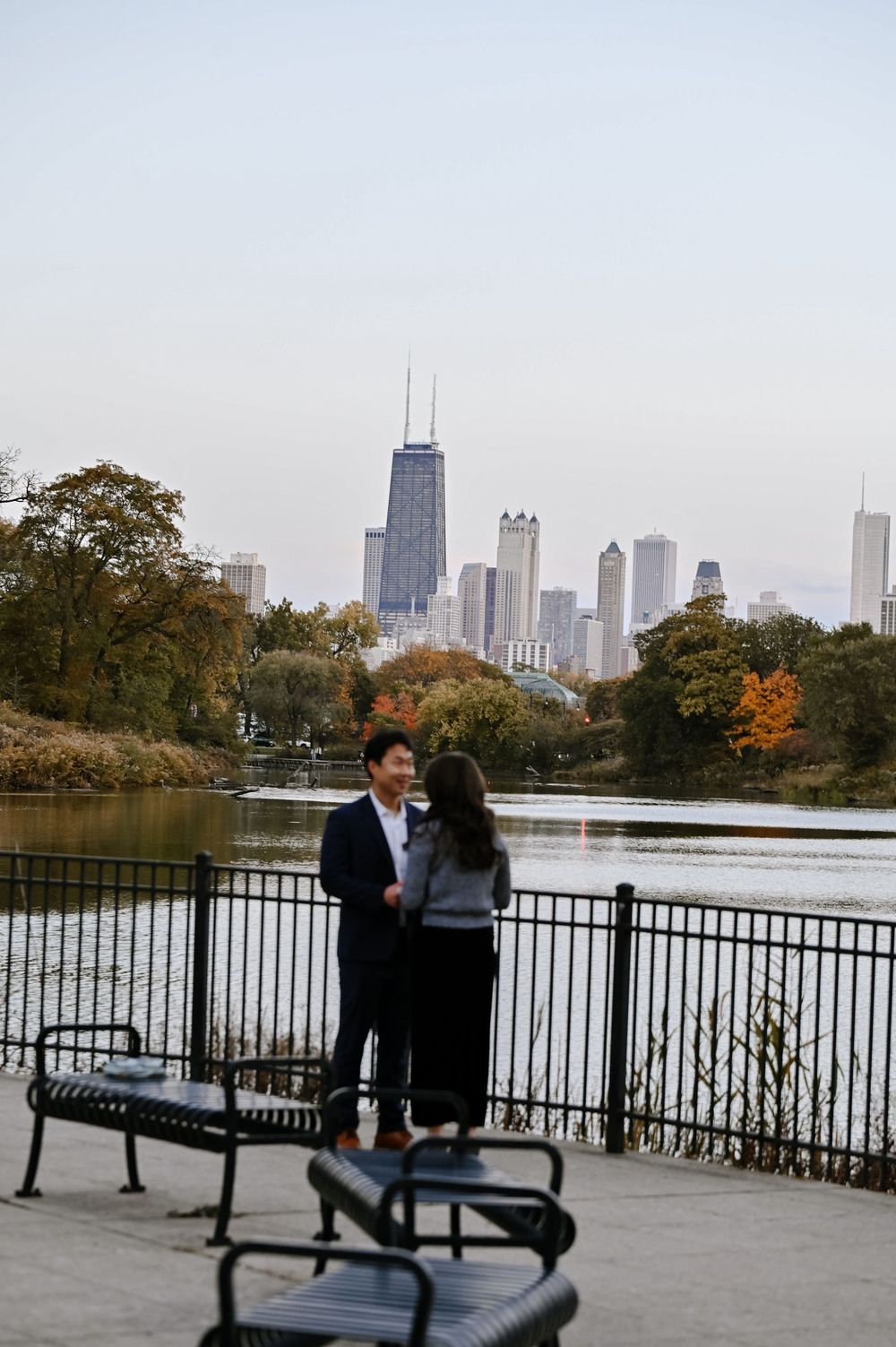 People relax on benches along a waterfront promenade with downtown Chicago's skyscrapers in the background.