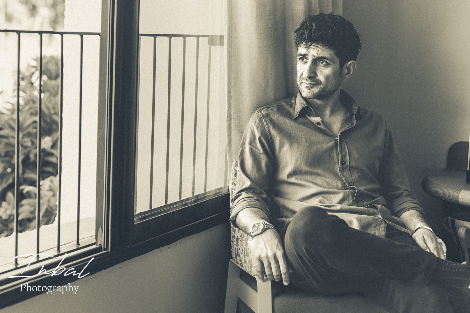 A black-and-white vintage old style photo of a man sitting near a window and looking outside in an hotel room in Marbella.