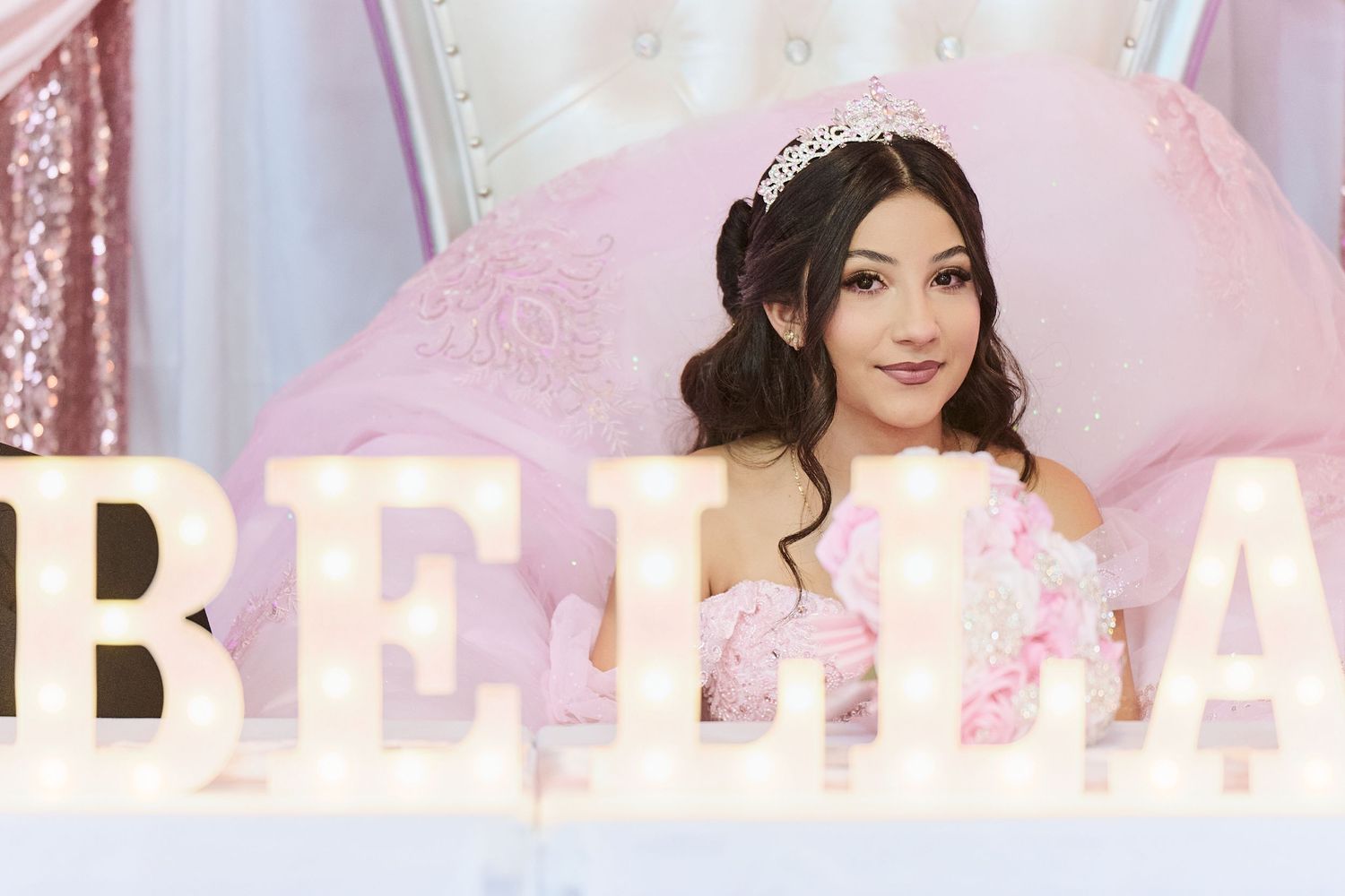 Woman in elegant black dress poses against pink and white floral backdrop at a formal event.