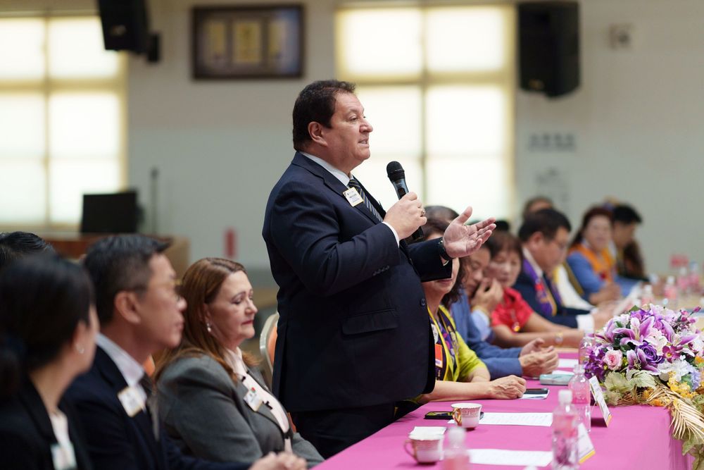 Business professionals seated at long tables during a conference or meeting with pink tablecloths and floral centerpieces.