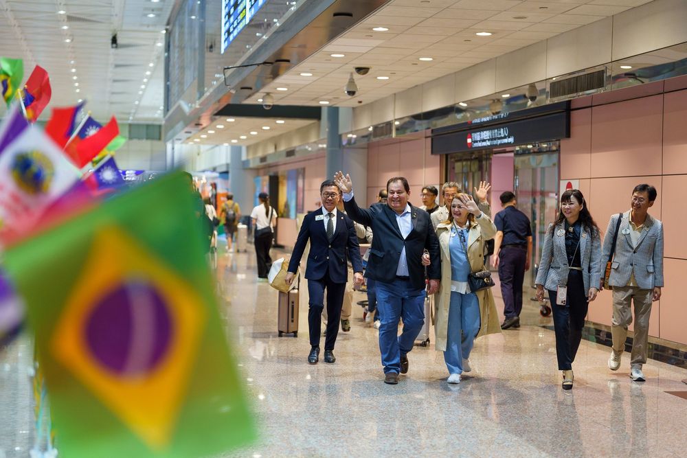 Busy airport terminal corridor with travelers walking through a modern concourse with bright lighting and retail shops.