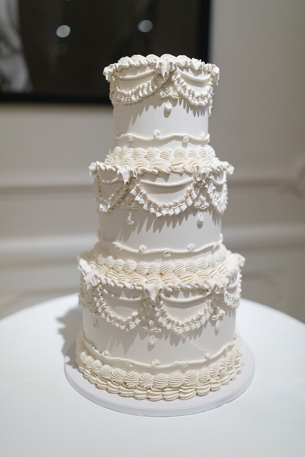 Elegant white wedding cake with delicate piped details and scalloped tiers displayed in multiple angles.