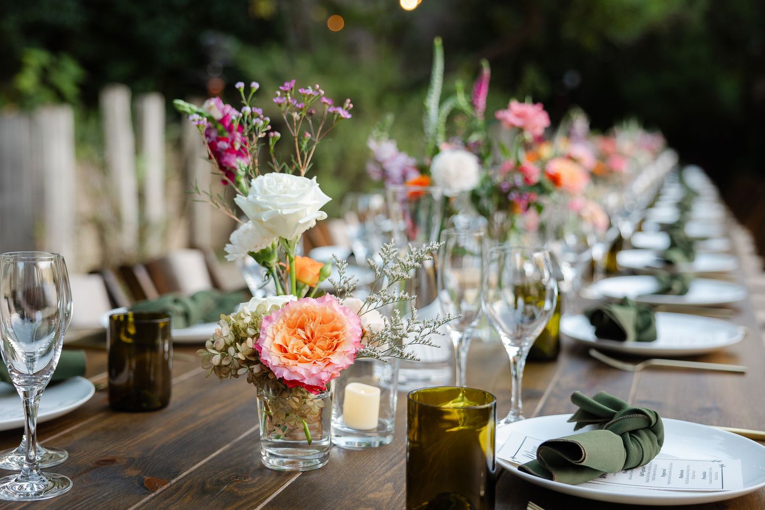 Elegant wedding reception table decor with soft pink roses, white daisies and delicate blue accents against a white tablecloth.