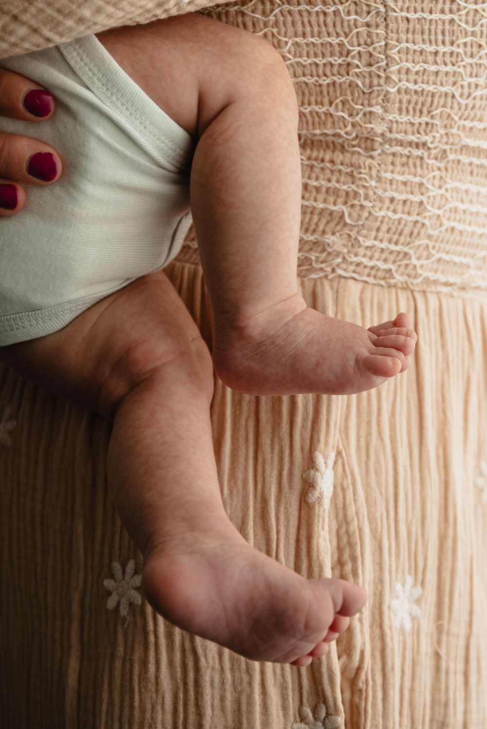 A series of baby's tiny feet against a textured beige fabric background showing different angles and details.