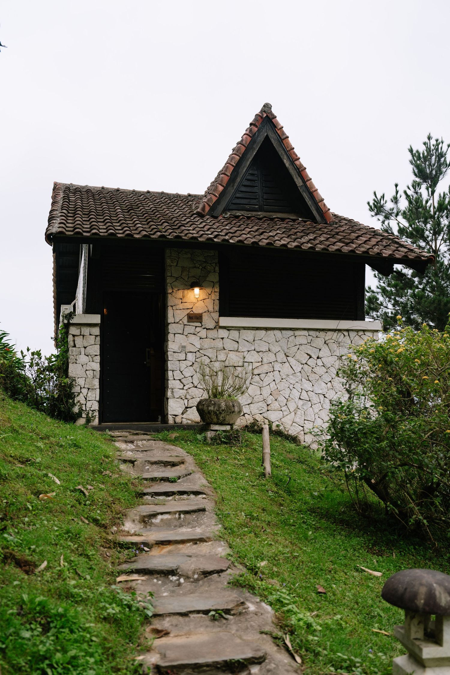 Rustic stone cottage with triangular tiled roof and stone pathway on grassy hillside.