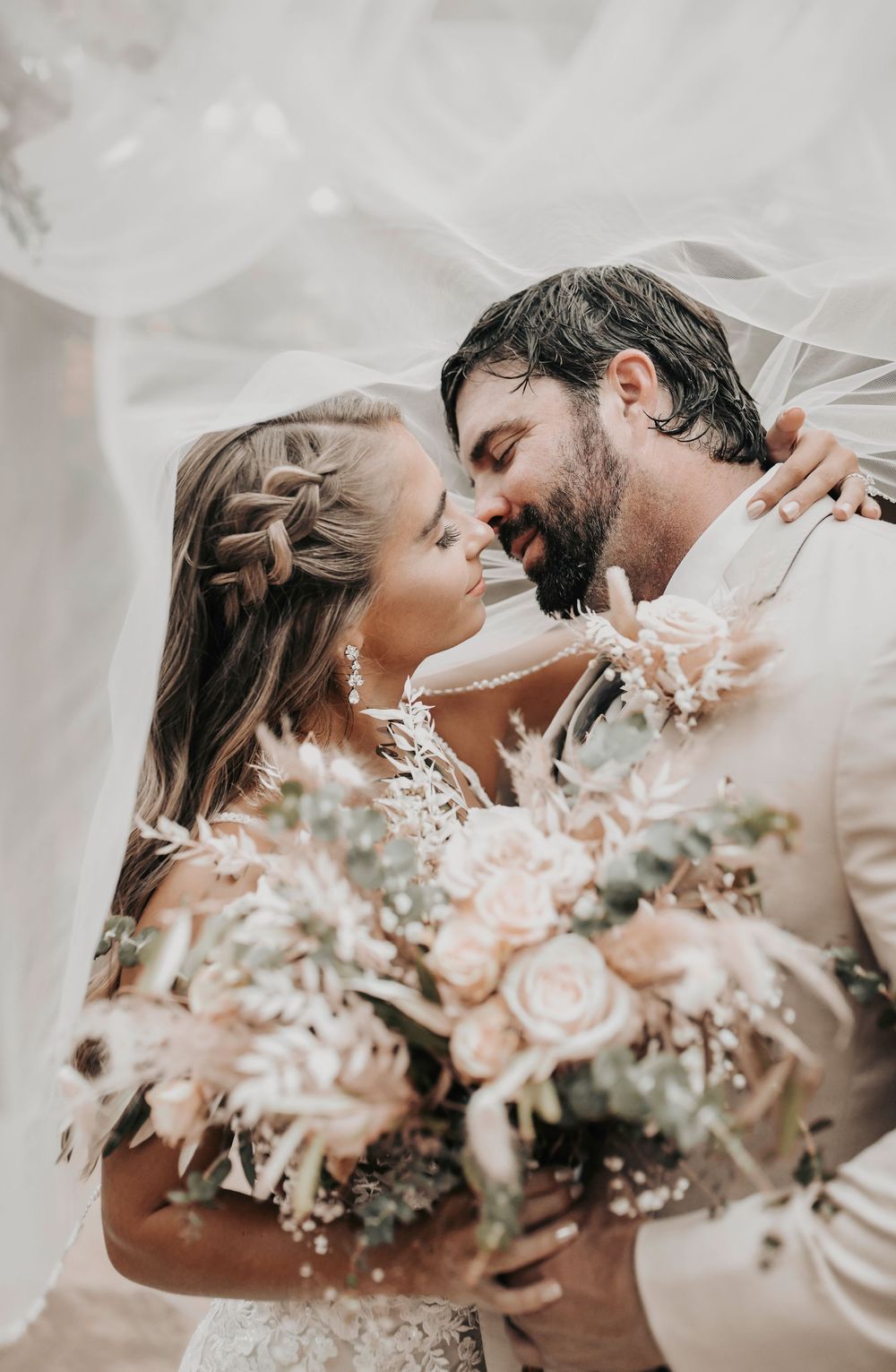 Bride and groom sharing a soft kiss under lace bridal veil with romantic lighting