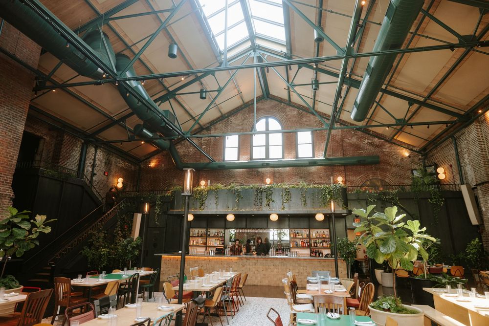 A modern rustic restaurant interior with exposed wooden beams, skylights, and hanging plants creates a bright, airy atmosphere Picnic Philly