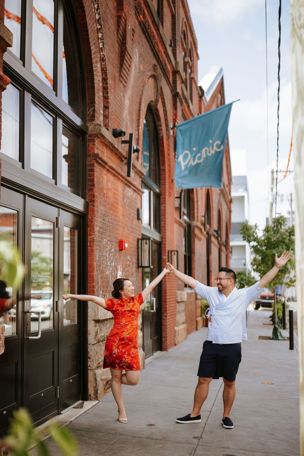 A couple dances playfully together on a brick-lined sidewalk outside historic buildings in an urban setting. Picnic Philadelphia