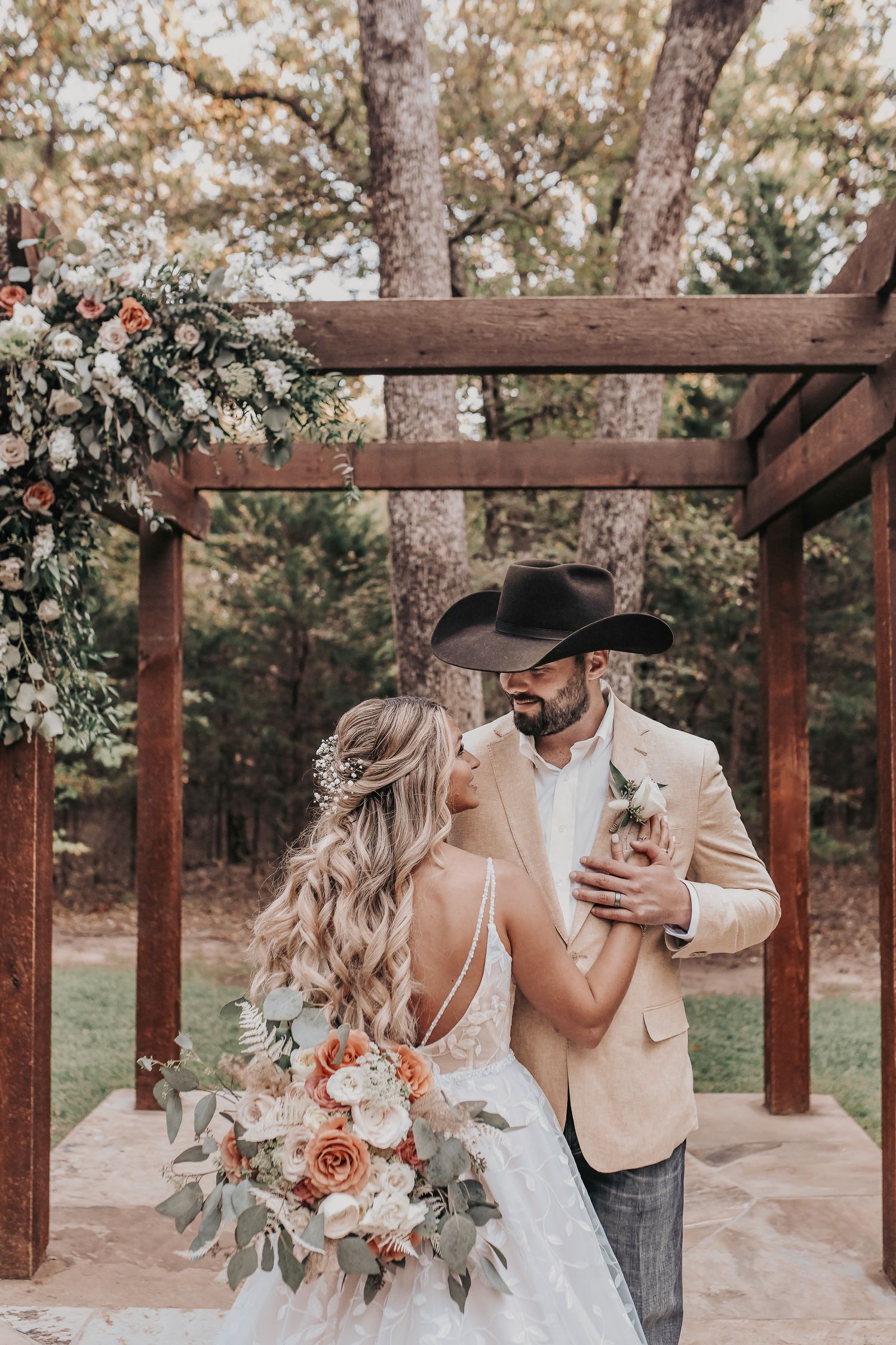 a groom holds his wife's hand as they smile at each other under their wooden altar in a grove of oak trees after their wedding ceremony