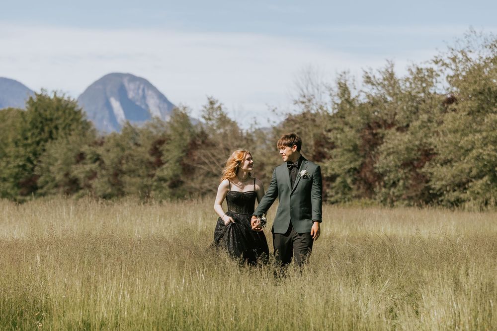 A romantic couple walking together through a golden meadow with mountains visible in the distance. Grad couple portraits