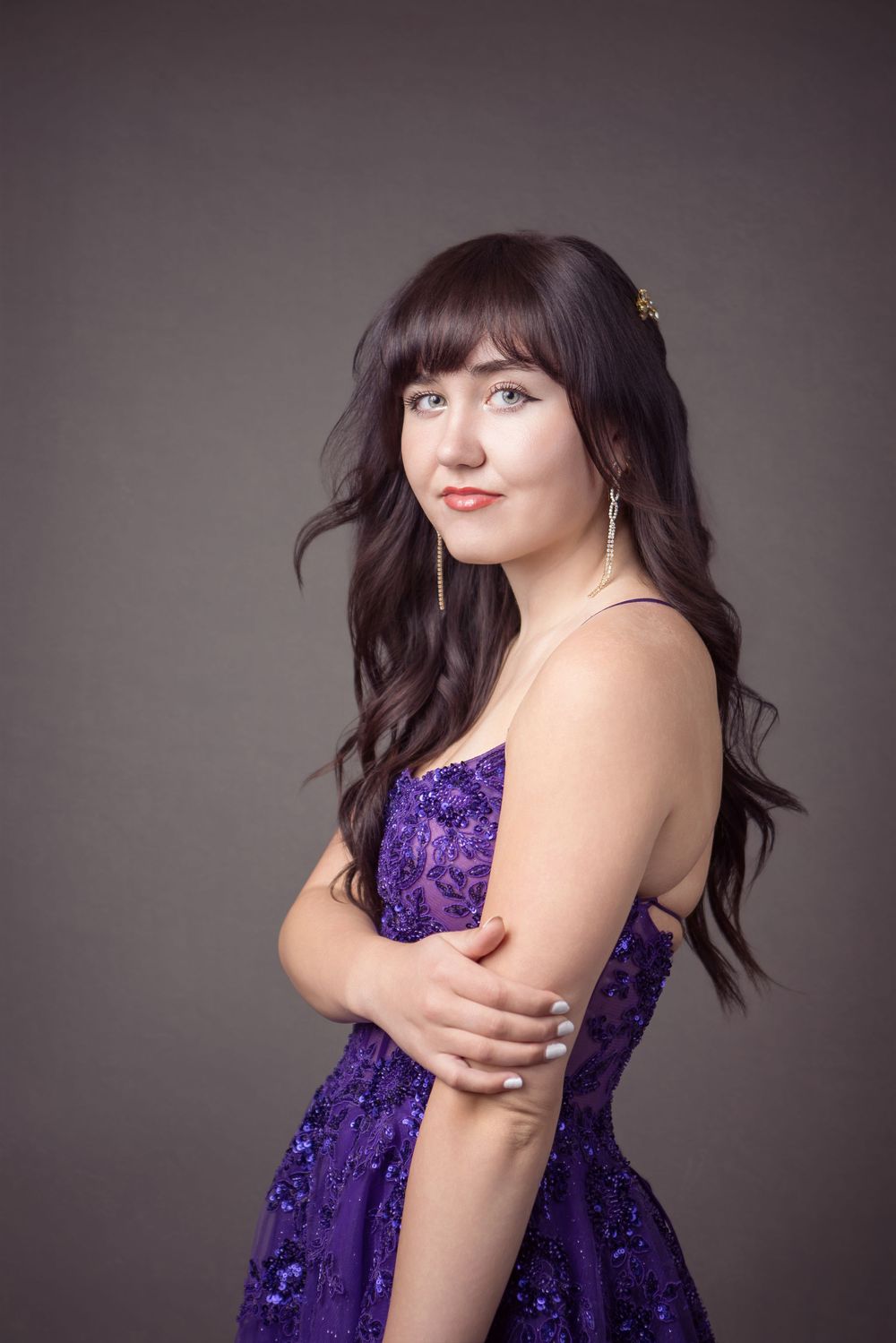 Studio portrait of figure in flowing deep purple sequin dress with graceful movement against gray backdrop.