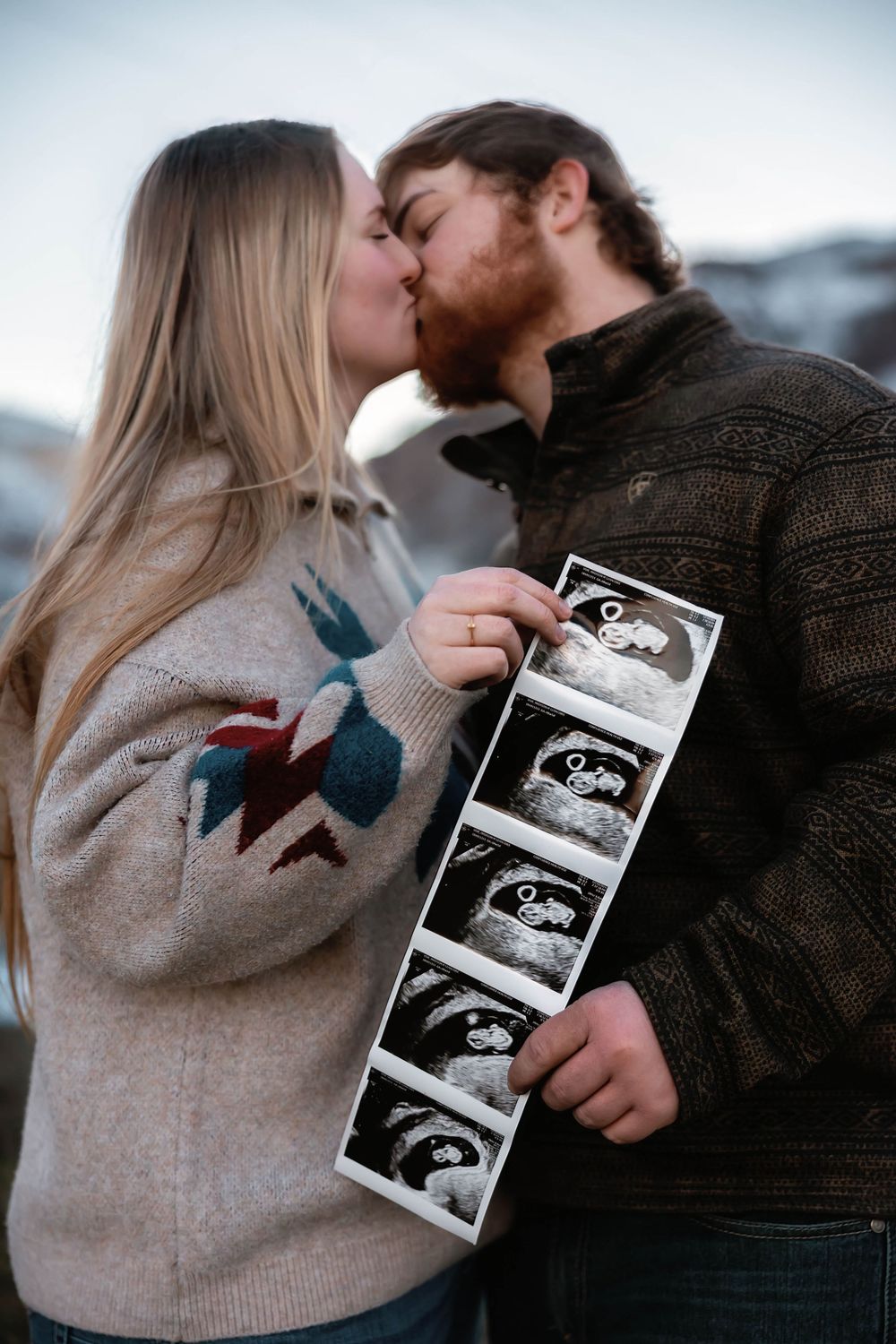 Couple shares intimate moment while holding ultrasound photos.