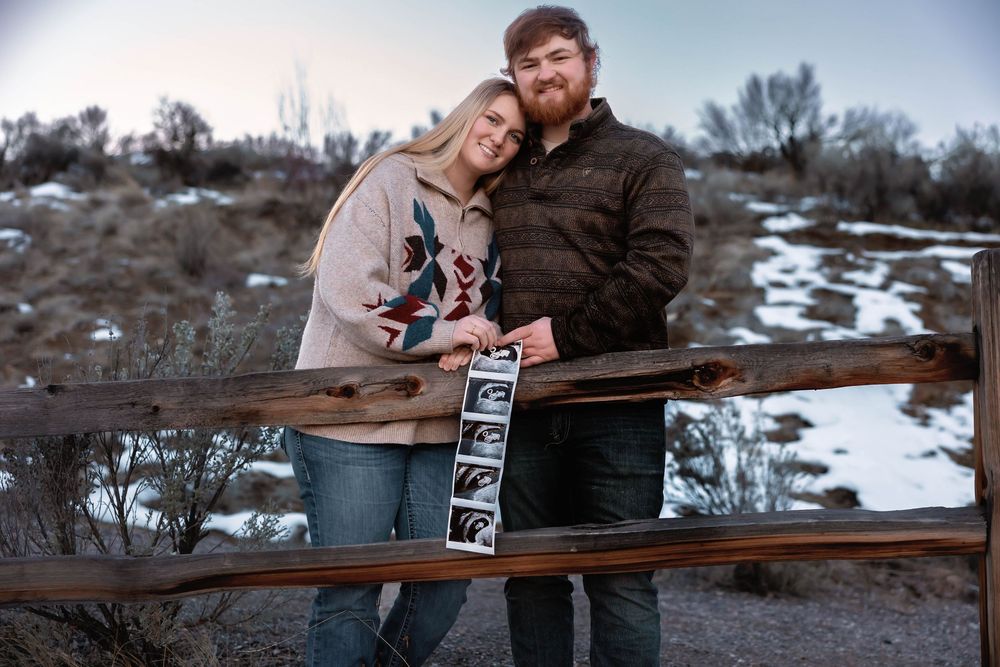 A couple shares a joyful moment on a wooden bench in a snowy mountain landscape.