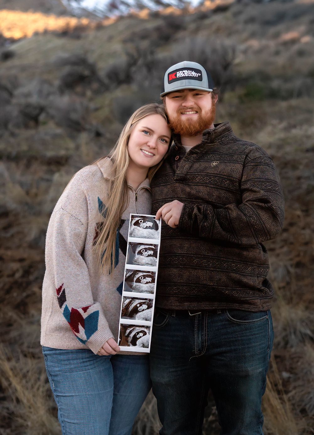 Couple poses with ultrasound photos during sunset pregnancy announcement shoot.