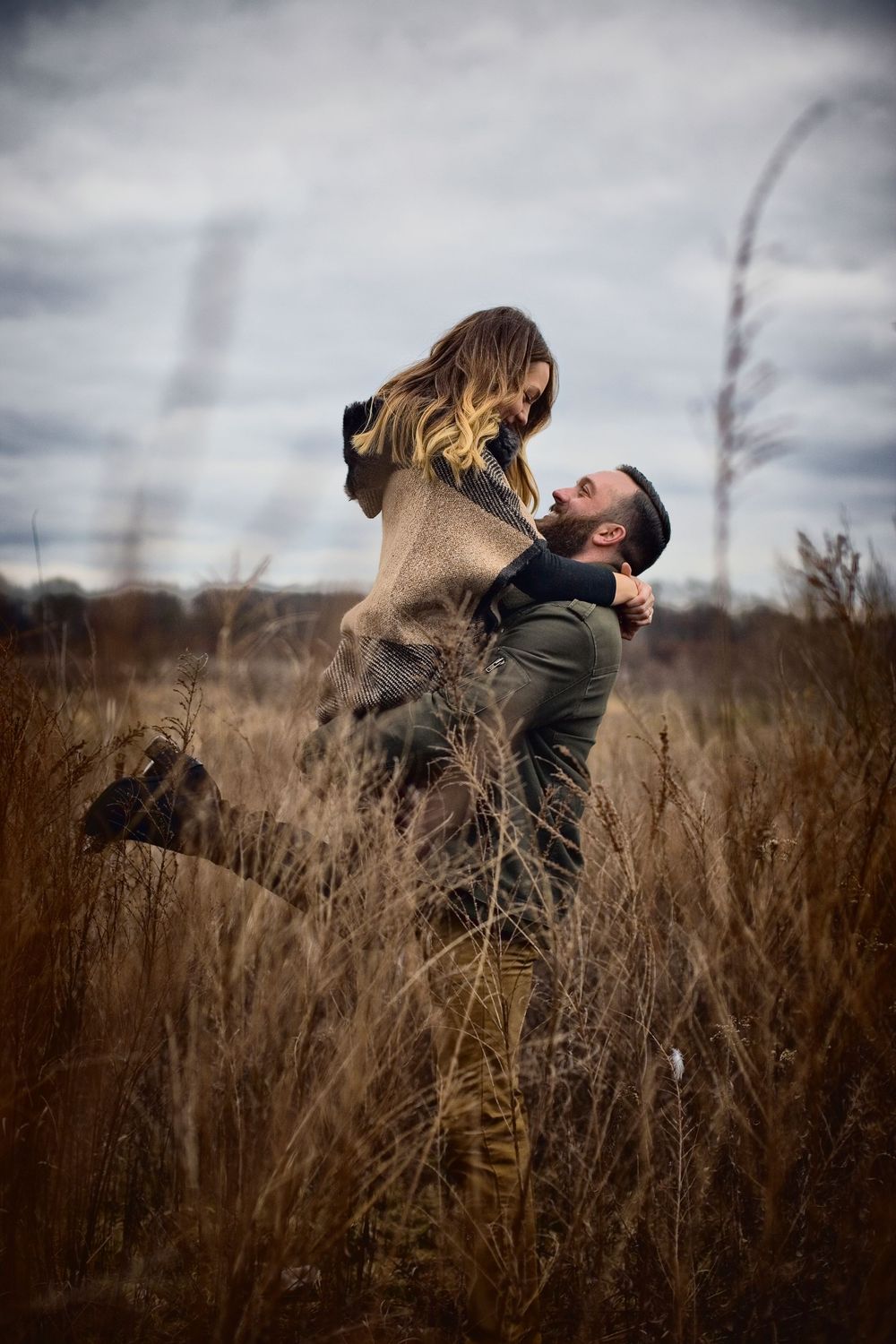 A couple embraces passionately in a golden field on a moody autumn day with stormy clouds overhead.