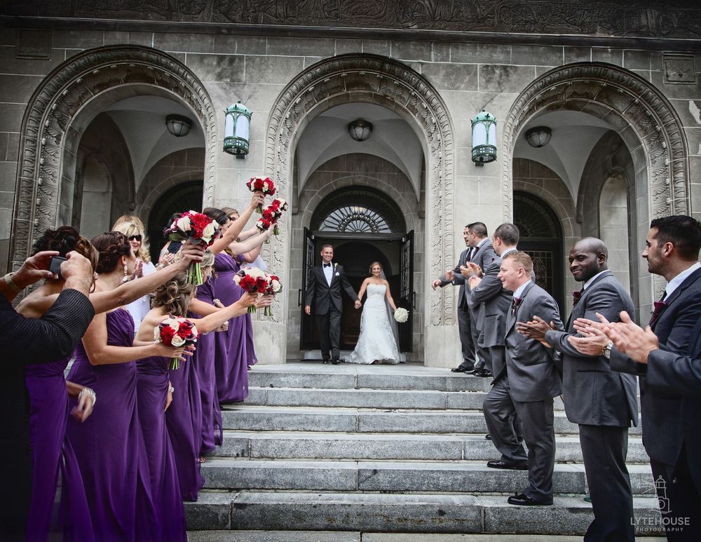 Wedding party members celebrate on stone steps wearing purple dresses and dark suits during festive wedding moment.