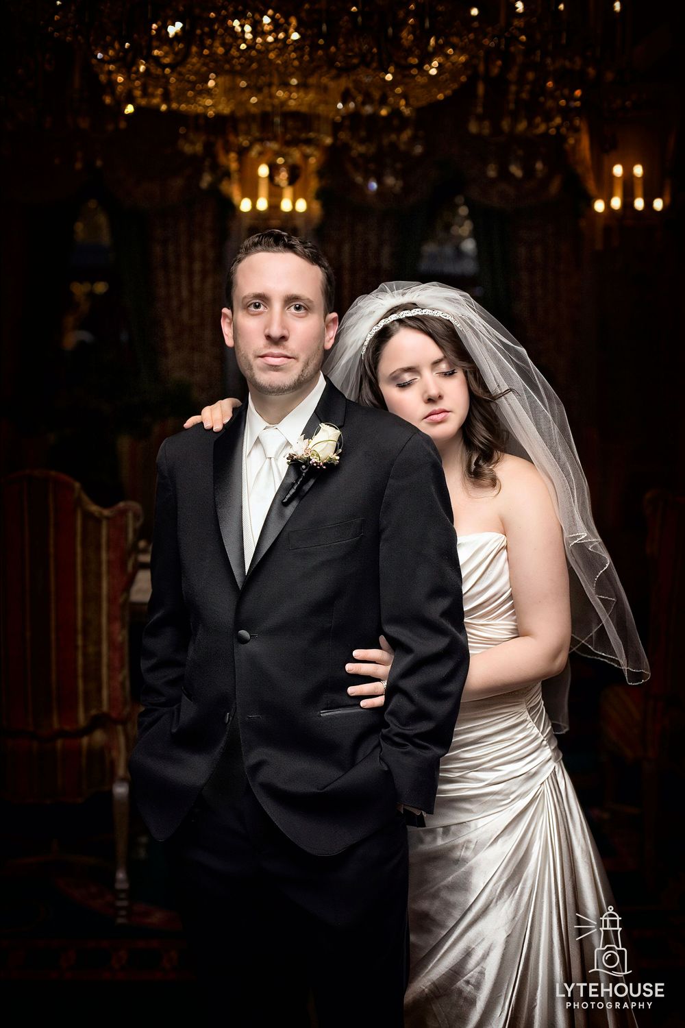 Wedding couple poses in a dimly lit venue with chandeliers, creating a romantic ambiance in their formal attire.